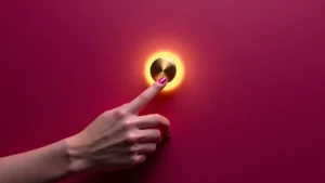 Imagen conceptual minimalista. Primer plano de una mano activando un interruptor dorado que simboliza el 'deseo por encargo' o responsivo. La imagen ilustra el concepto de 'cómo aumentar el deseo' y desmiente el 'mito espontaneidad sexual' frente a la 'falta de deseo sexual' pasiva. Tono sensual y elegante con fondo magenta.